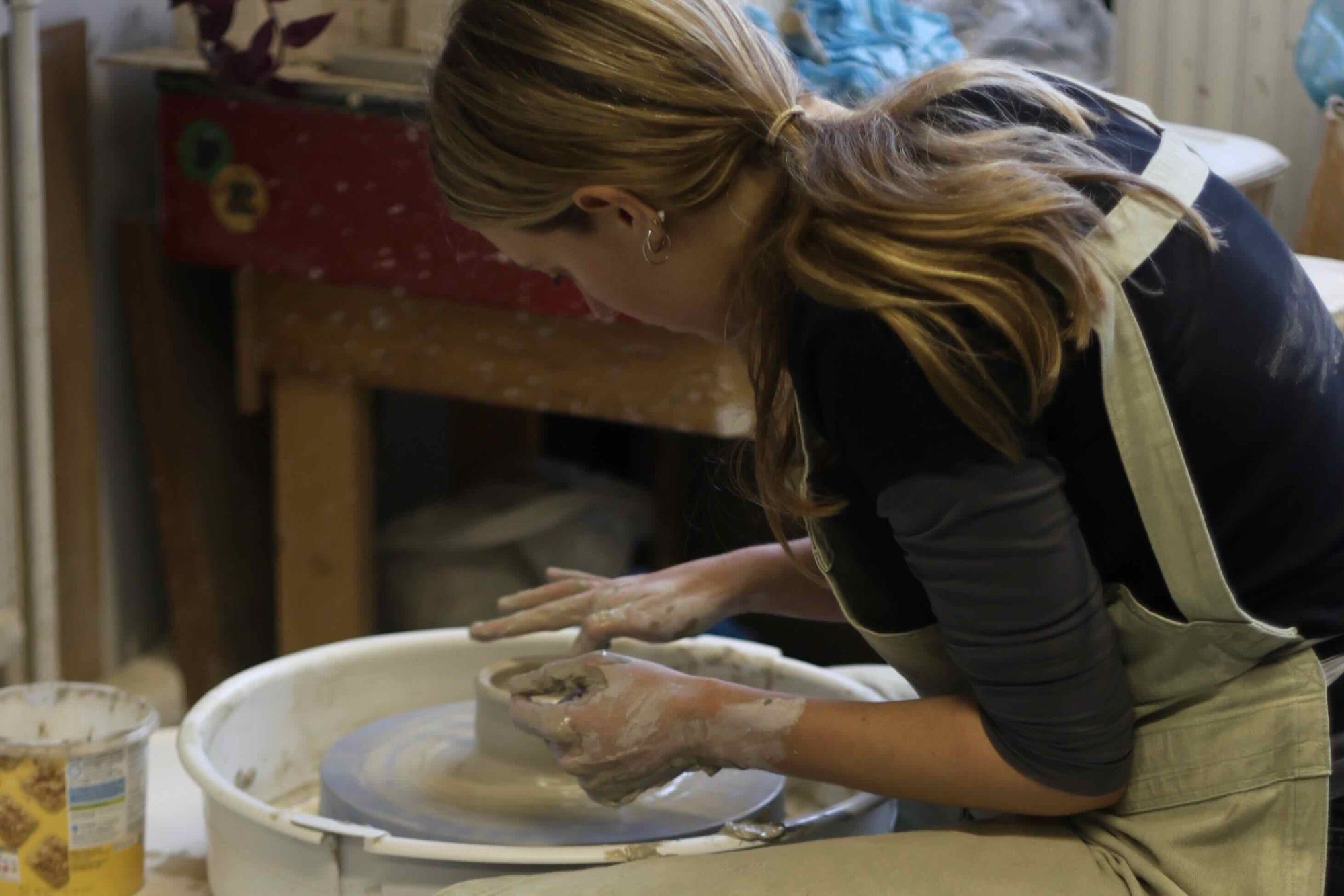Person seated at a potters wheel throwing a ceramic form