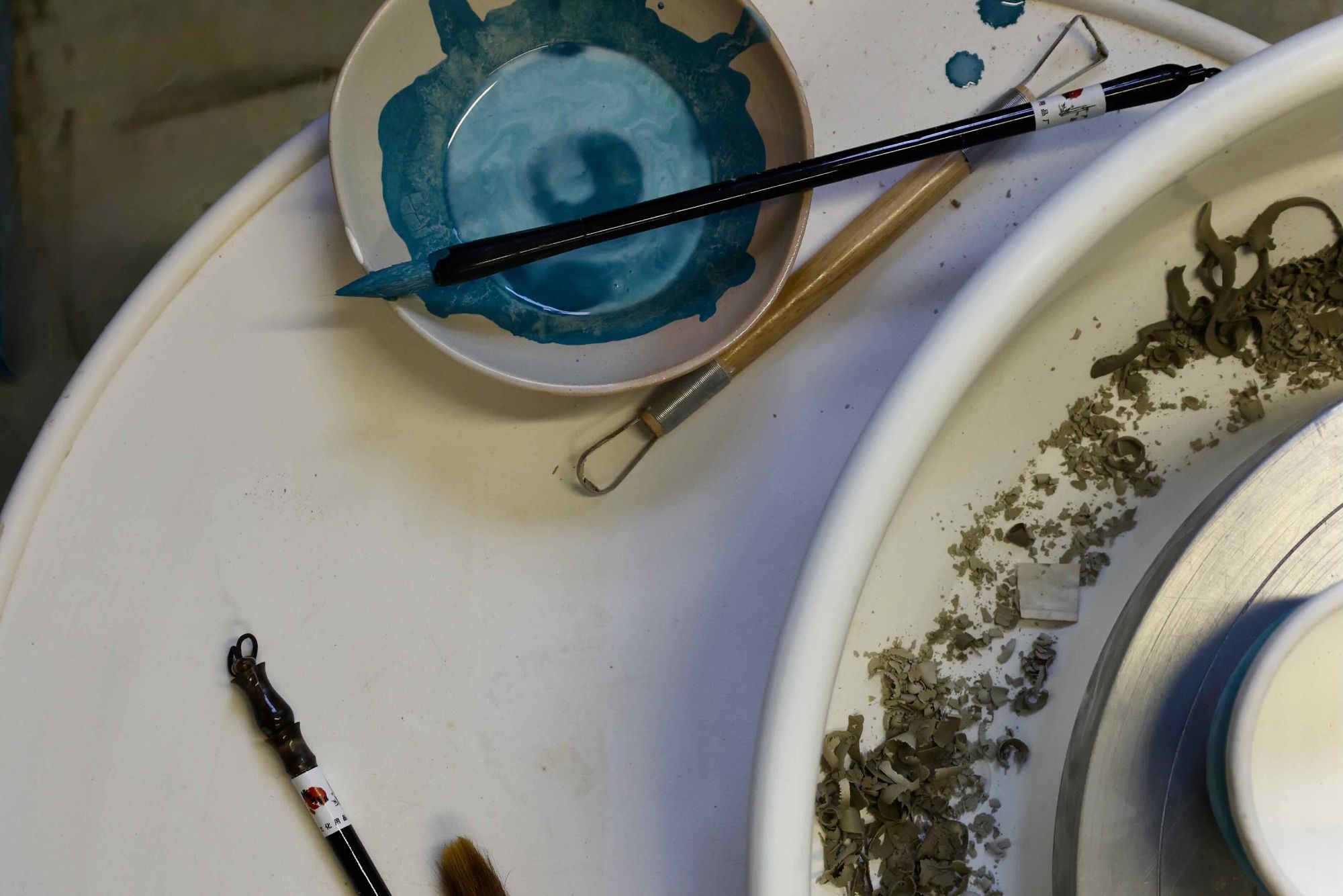 Potters wheel with paint brushes and glaze in a small bowl