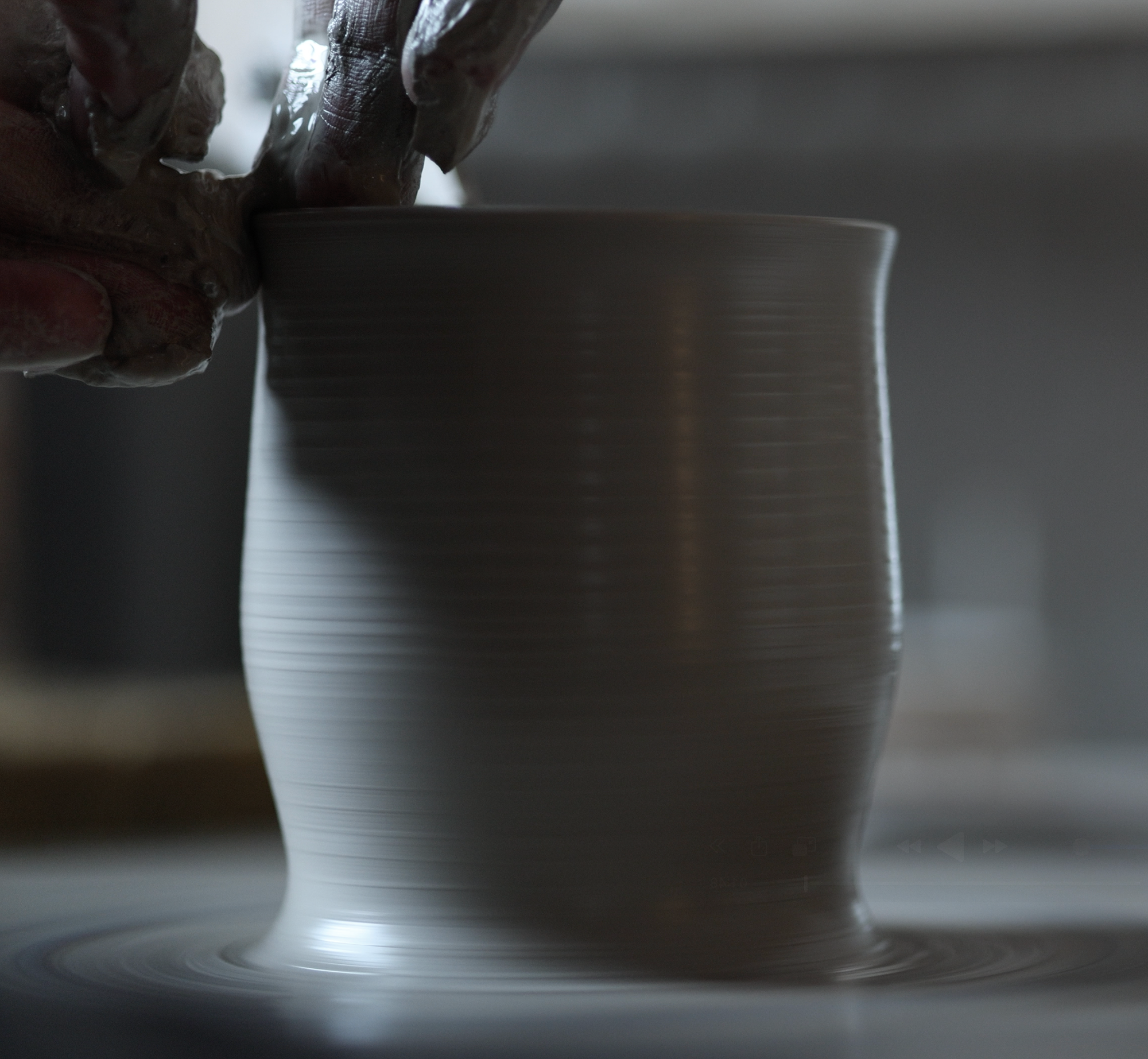 Soft clay form on potters wheel, hands forming shape and holding a sponge