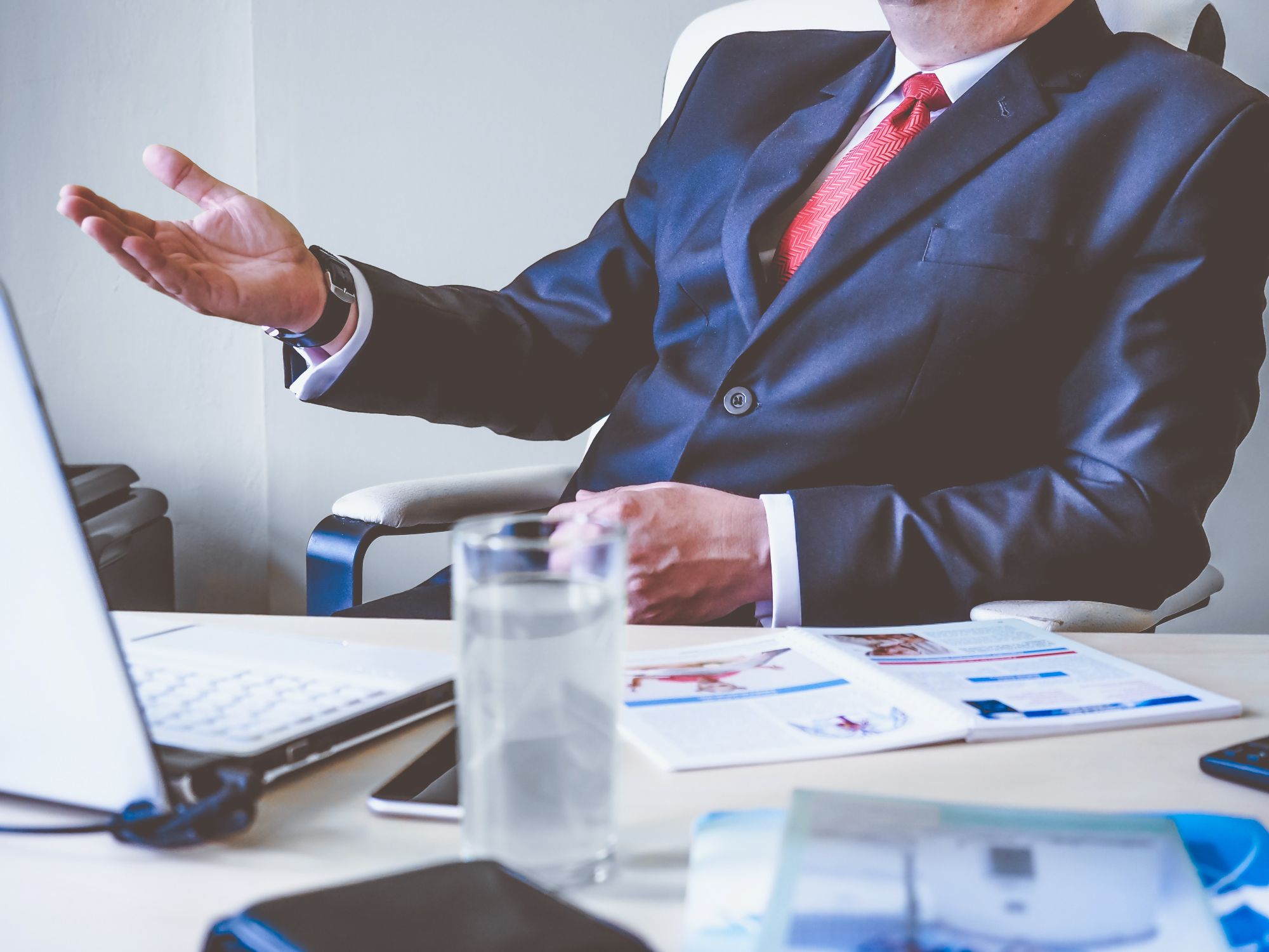 Being impactful - Bodyshot of a man in a suit sat at a cluttered desk, talking