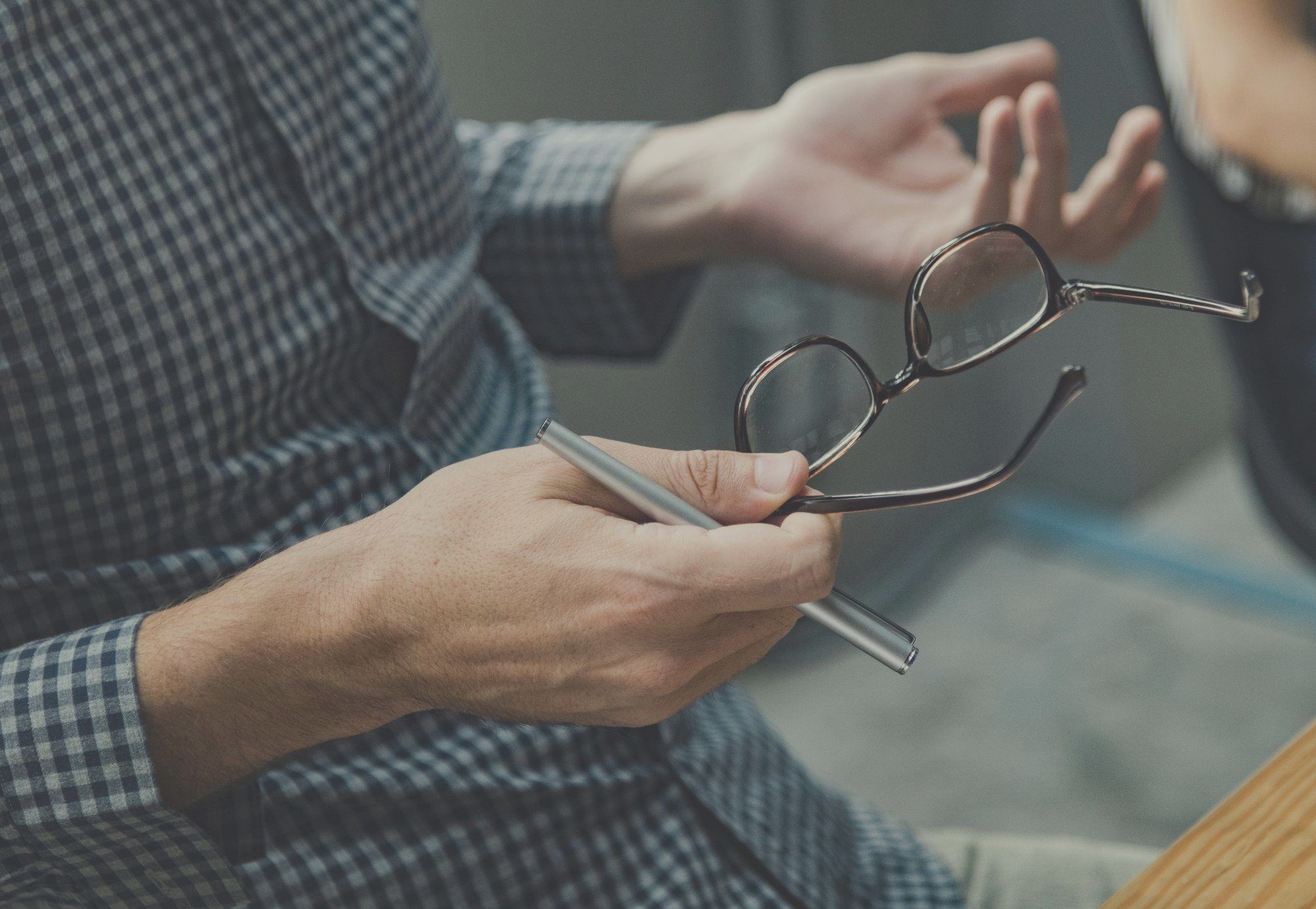 How? - A man's hands holding glasses and a pen, seeming to be asking a question