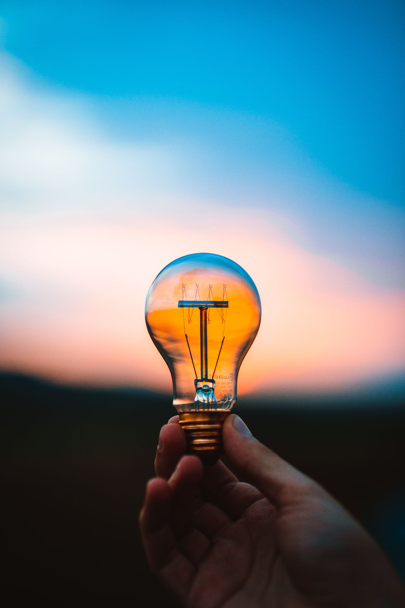 Close up of someone holding a lightbulb with the sun setting in the background