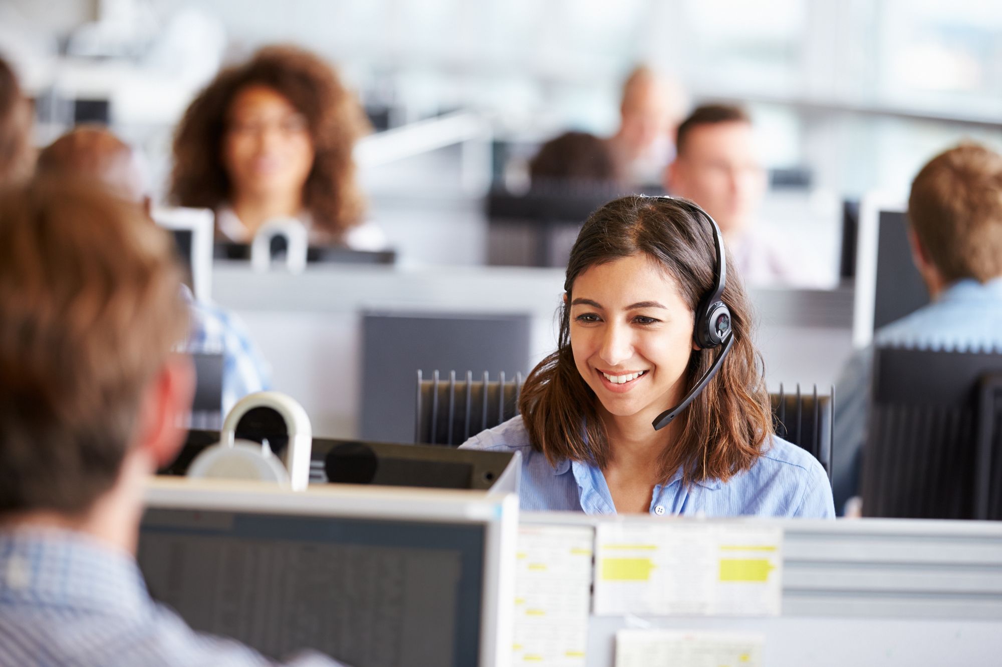 Being of value - a smiling girl in an office, looking at her computer with a headset on