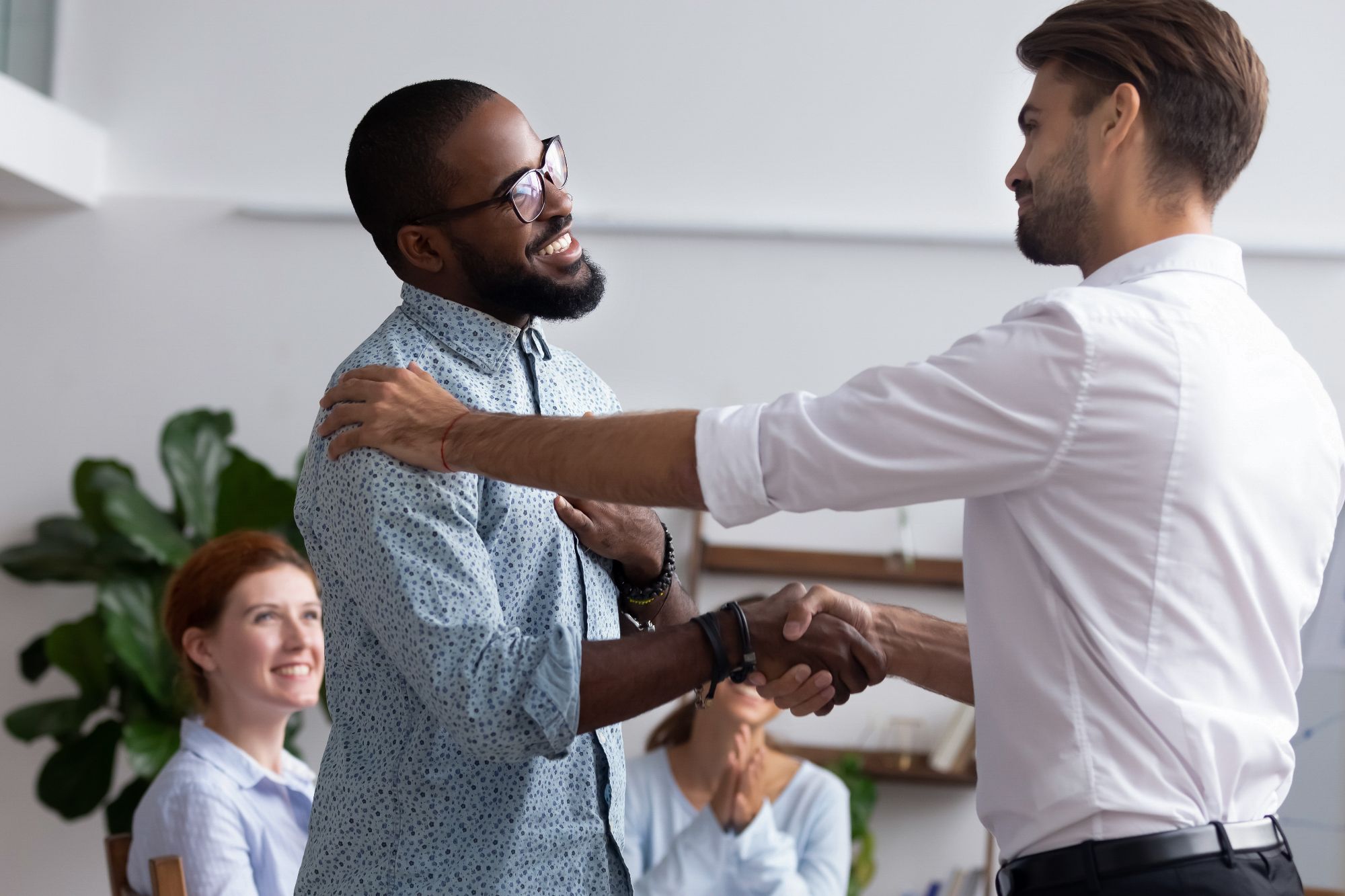 Two men happily shaking hands, one has his hand on the other's shoulder