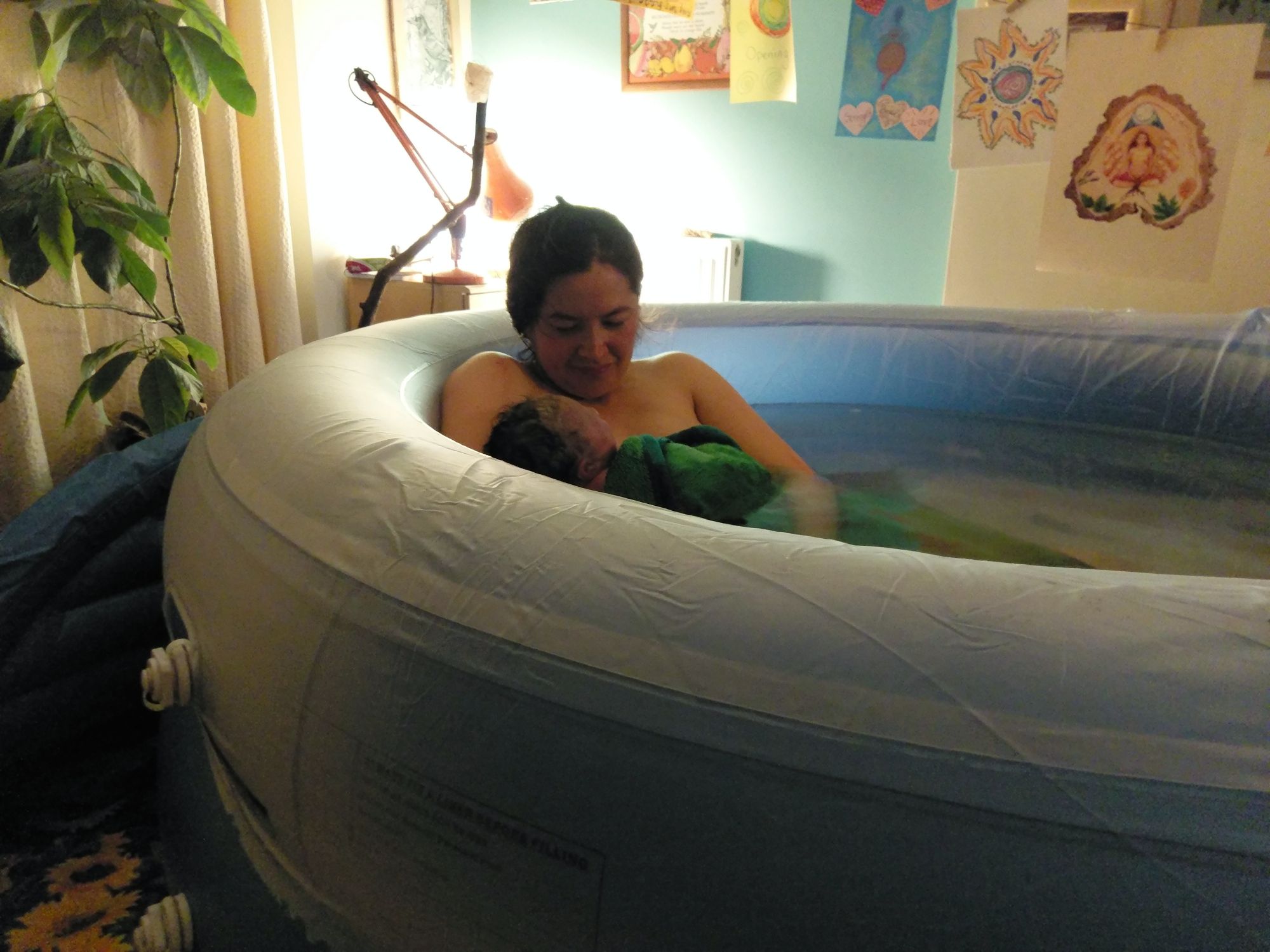 A woman sits in a birth pool and gazes lovingly down at her new baby.