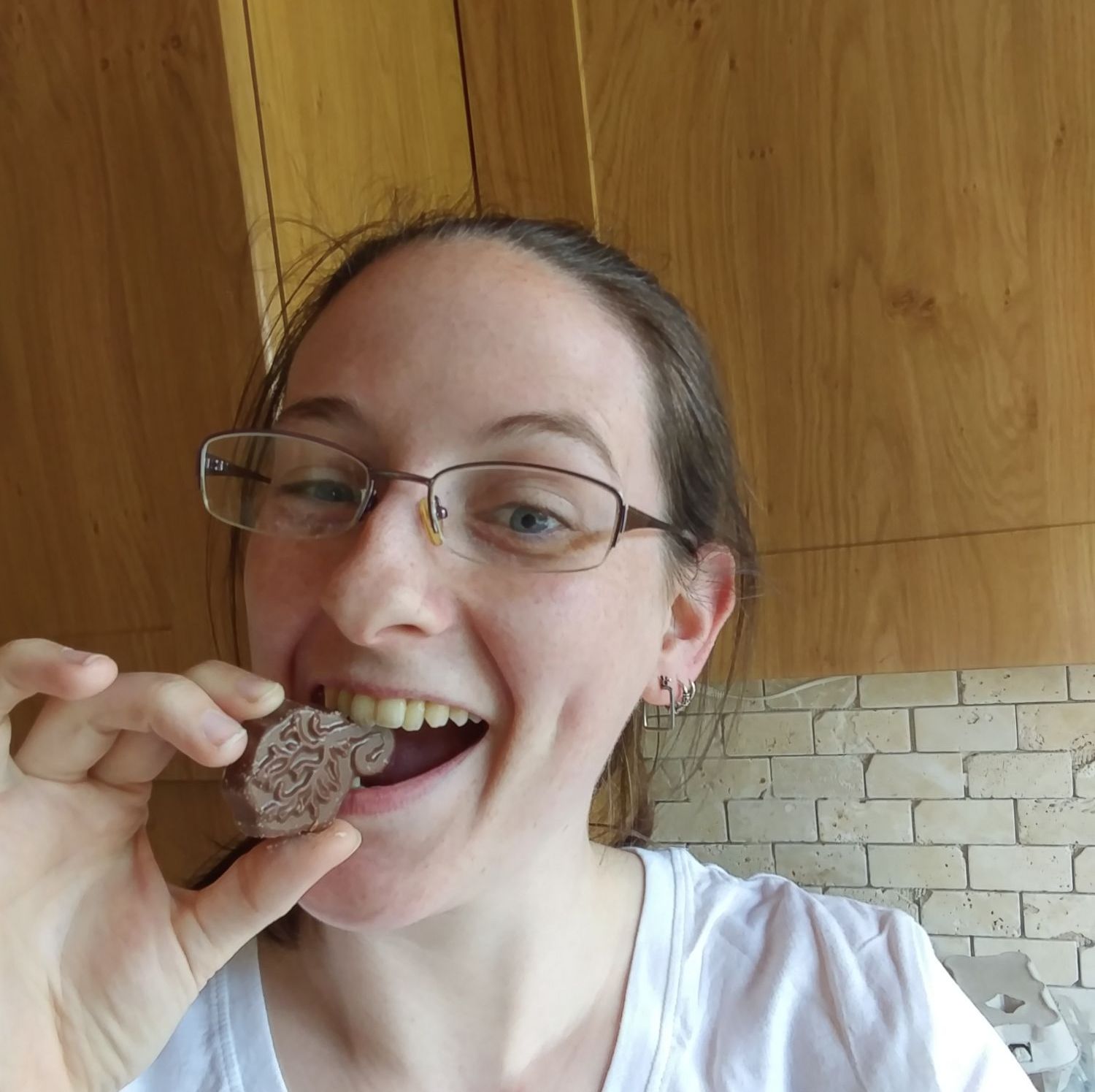 An image of Caz with kitchen units in the background behind her. She is eating a chocolate shaped like a placenta.