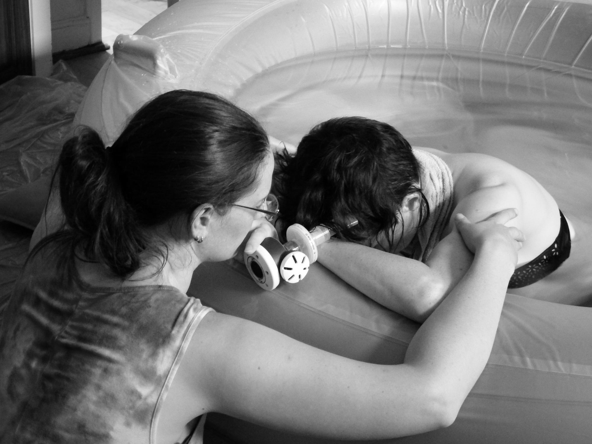 A woman labouring in a birth pool. Caz is providing physical touch over the side of the pool as she rests between contractions.