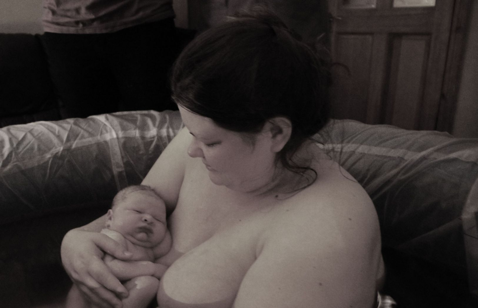 Black and white image of a woman in a birth pool holding her newborn baby.