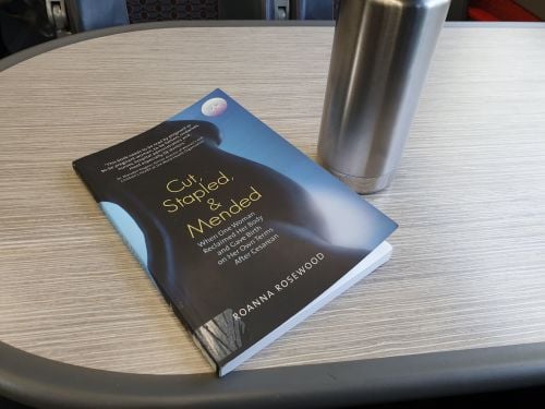 An image of the book next to a travel mug on a train table.