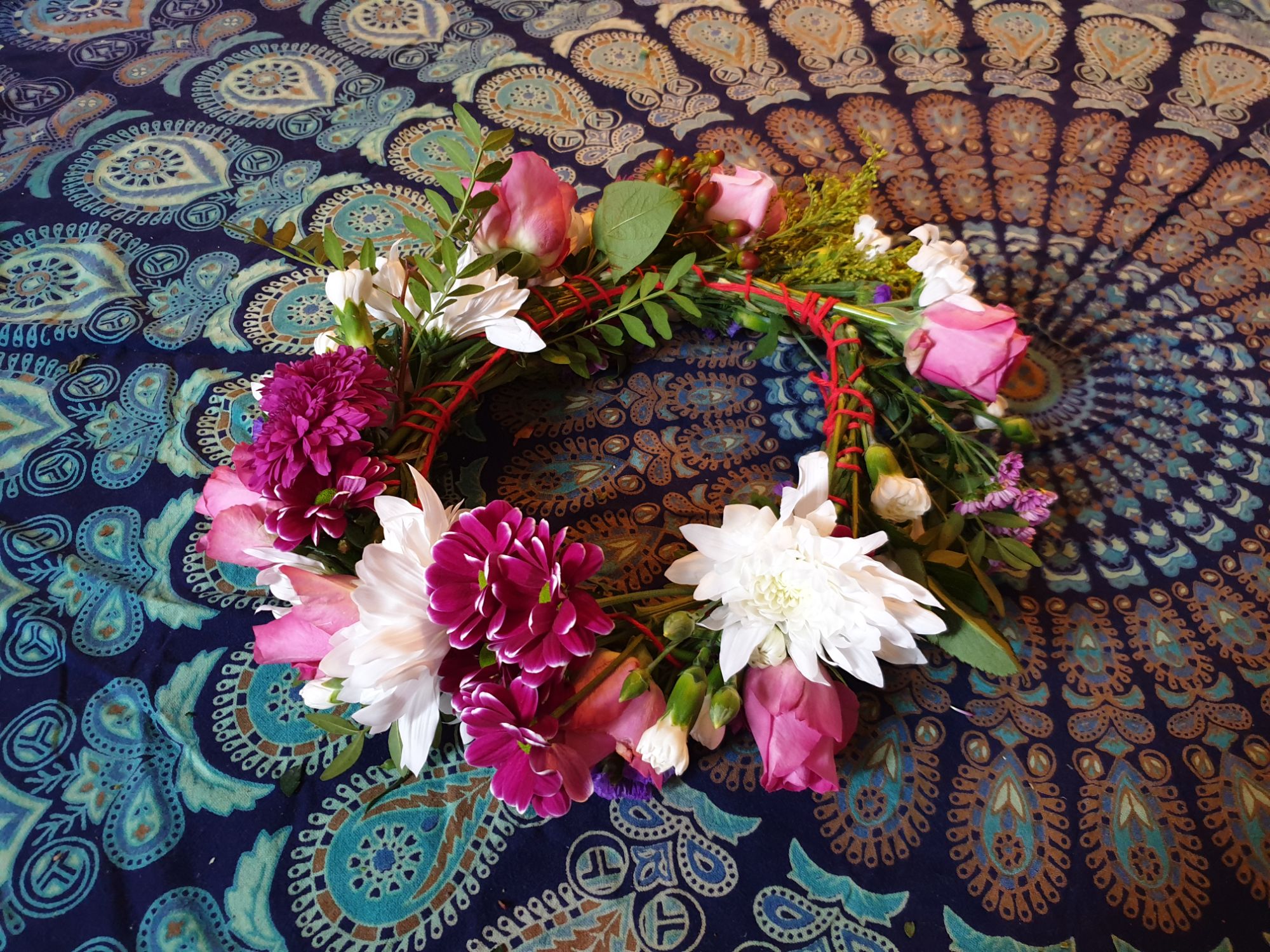 A flower crown made from fresh flowers. The flowers are pink, purple and white and woven together with yarn.