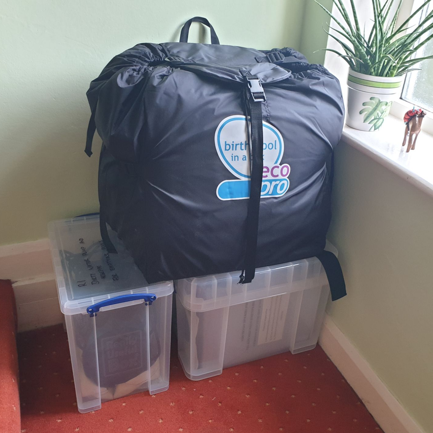 2 lidded plastic boxes on the floor, with a birth pool in a storage bag on top of them.