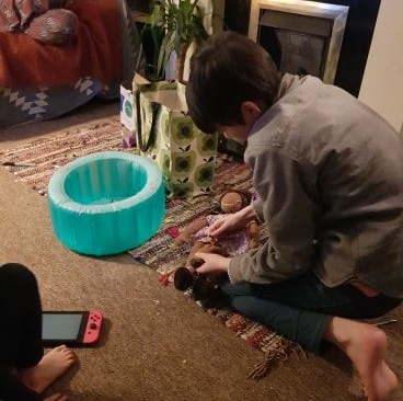 Image of a child playing with a doll that gives birth. An inflatable doll birth pool waits in front of him.