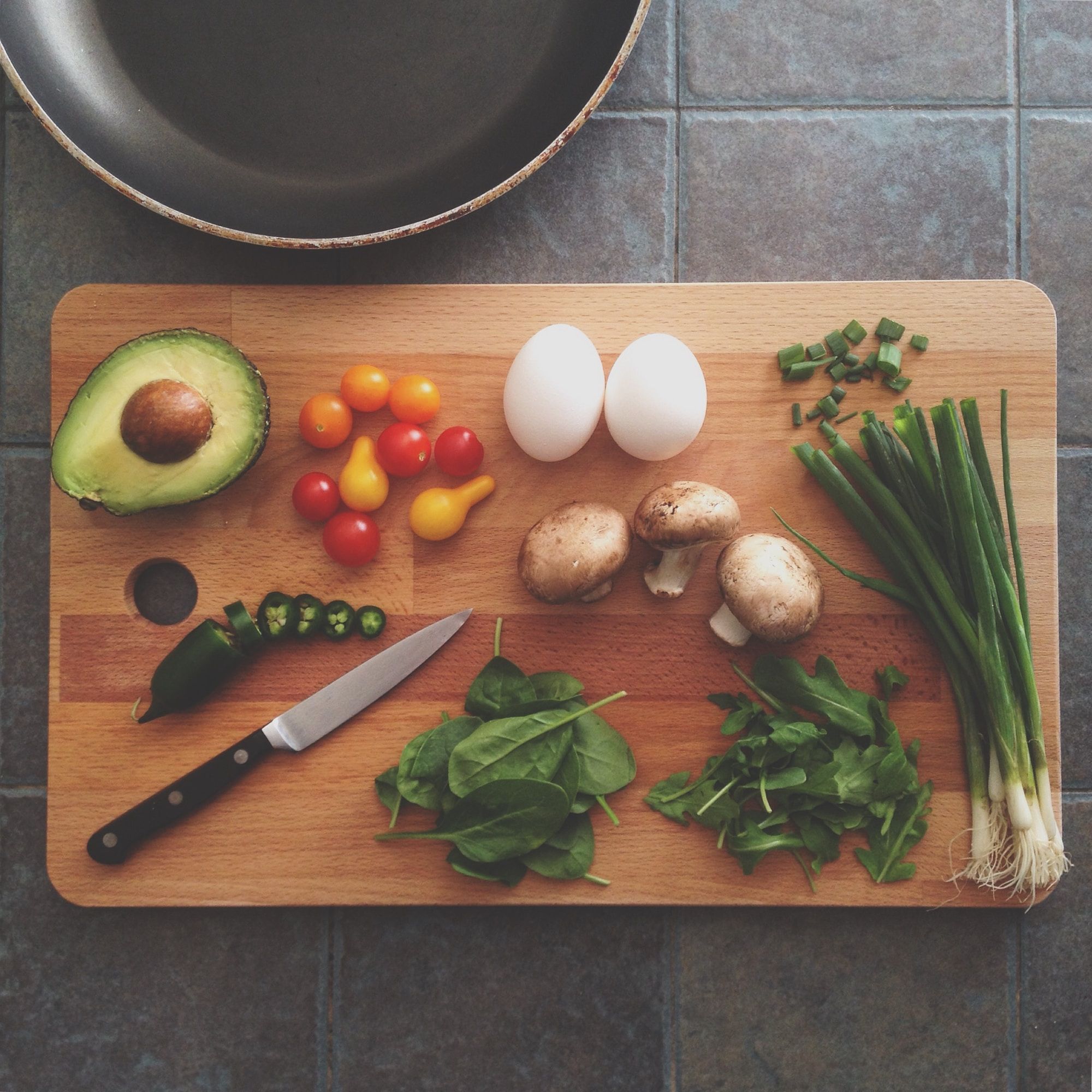 Flatlay image of various meal ingredients on a chopping board. A frying pan is nearby.