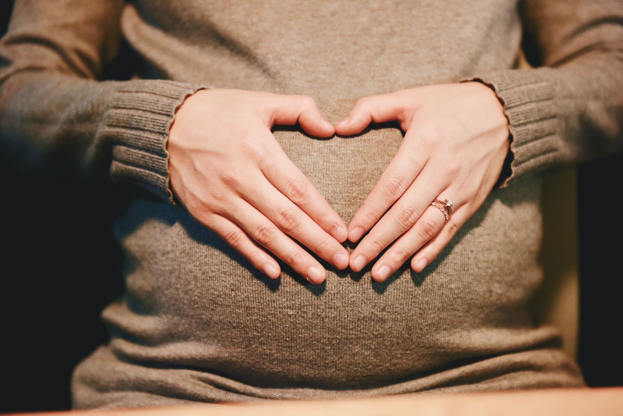 Image of a hands forming a heart shape over a pregnant belly
