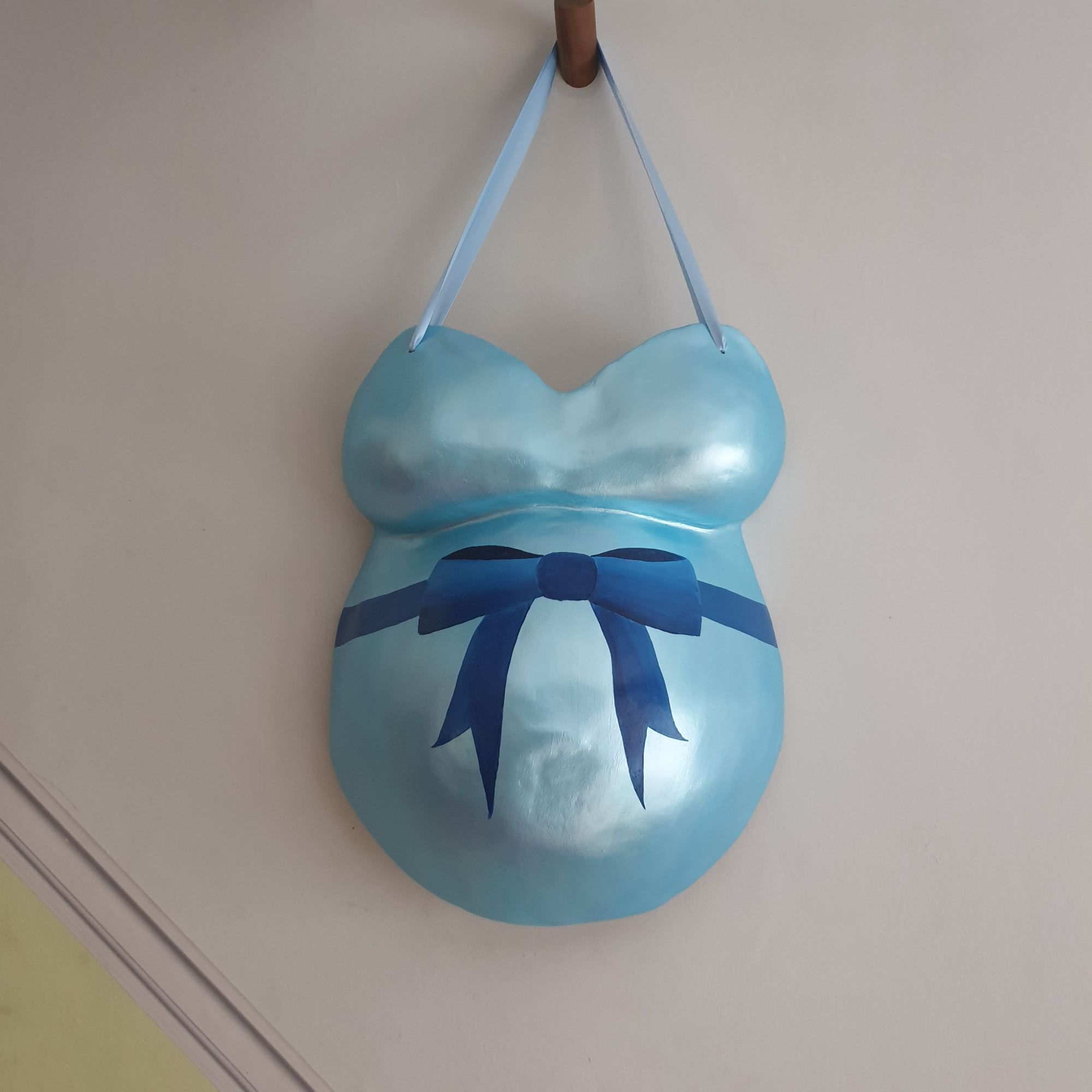 The finished cast, with a blue bow painted on it, hanging on a wall.