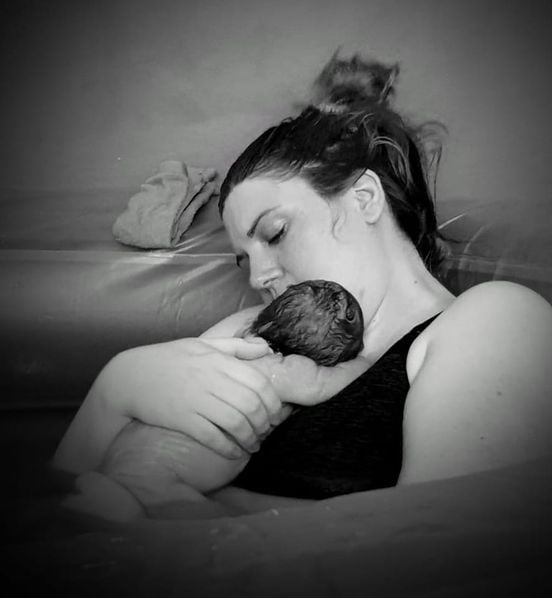 Black and white image of a woman holding a newborn baby on her chest in a pool.