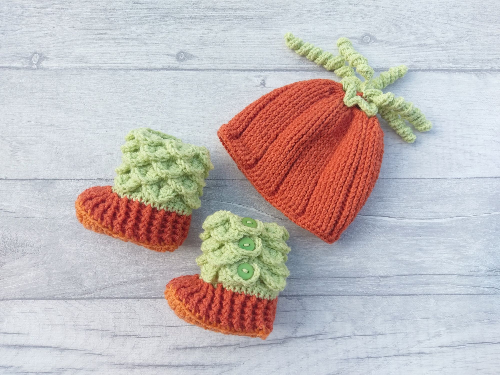 A flat lay of a hat and bootie set, made with orange and green yarn and made to look like a pumpkin.