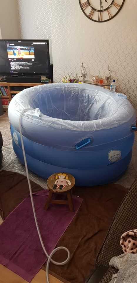 A mini pool being filled in a client's living room. The filling hose is draped over the side and there is a wooden stool in front of the pool for access.