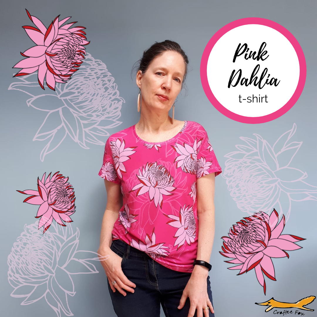 Bright pink ladies tshirt with big, bold pale pink and red Dahlia flowers. The t-shirt has a rounded neck, short sleeves. It is worn by a 40 plus year old woman, who is wearing jeans. Surrounding the woman are images of the Dahlias. A cricle reads 'Pink Dahlia' t-shirt