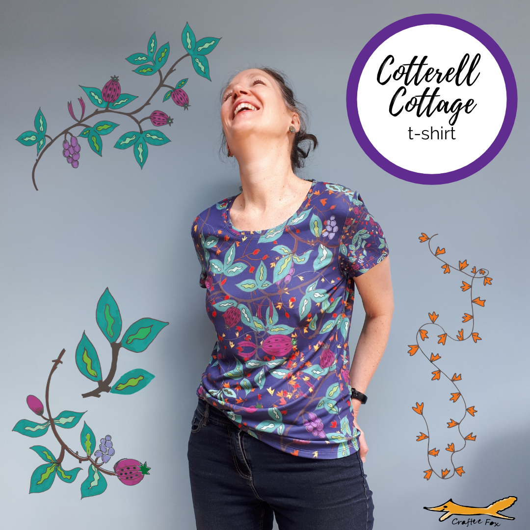 A 40 year old plus woman is laughing, wearing a dark purple/blue t-shirt that is covered in leaves, vines and large purple fruits. These vines and plants are surrounding the woman on the image and a circle reads 'Cotterell Cottage' t-shirt
