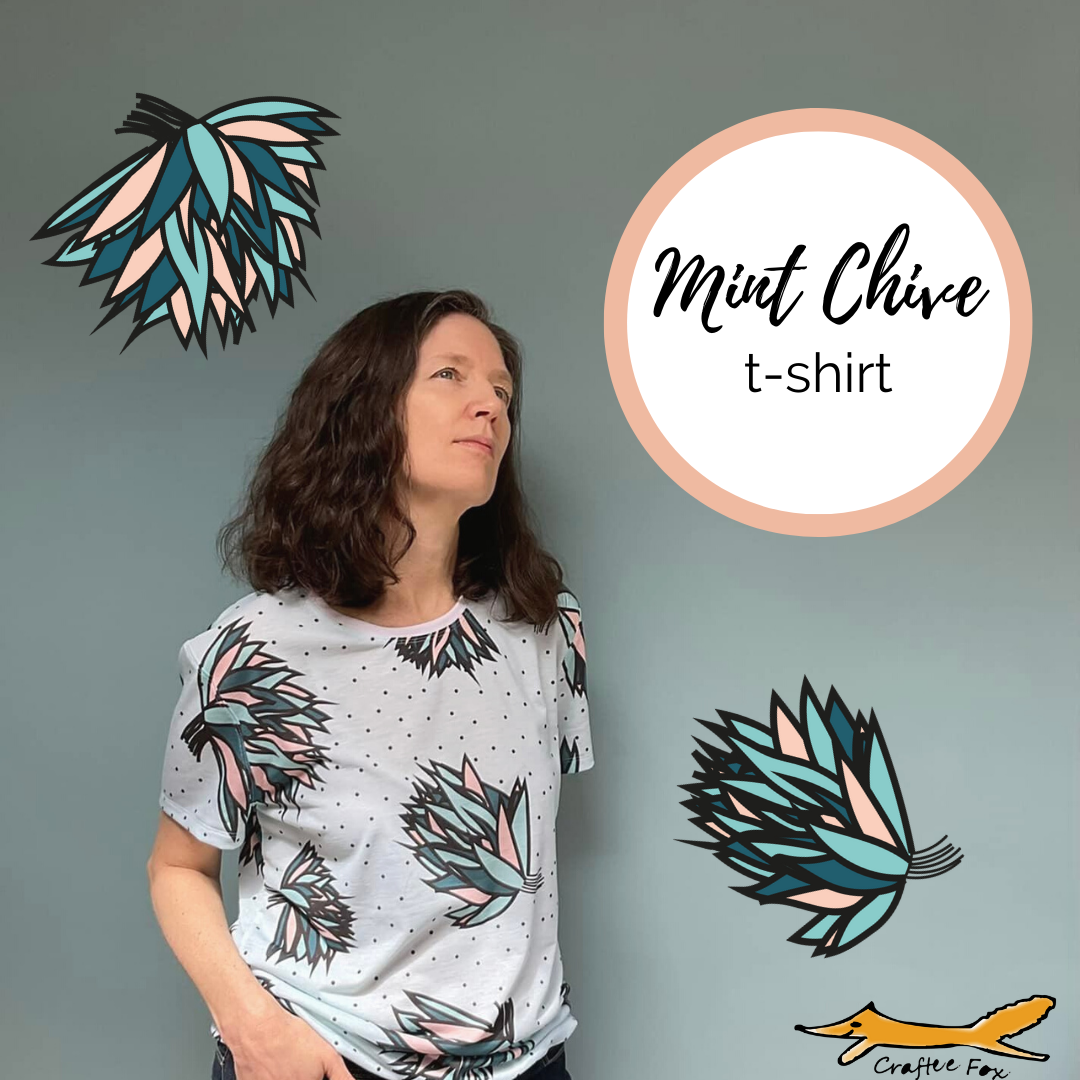 A 40 year old plus woman wears a mint green/pale blue tshirt which has large, bold flowers on. The petals of the flowers and greens and peach coloured. There are two flowers printed onto the  image surrounding the woman. A cirle reads 'Mint chive t-shirt'.
