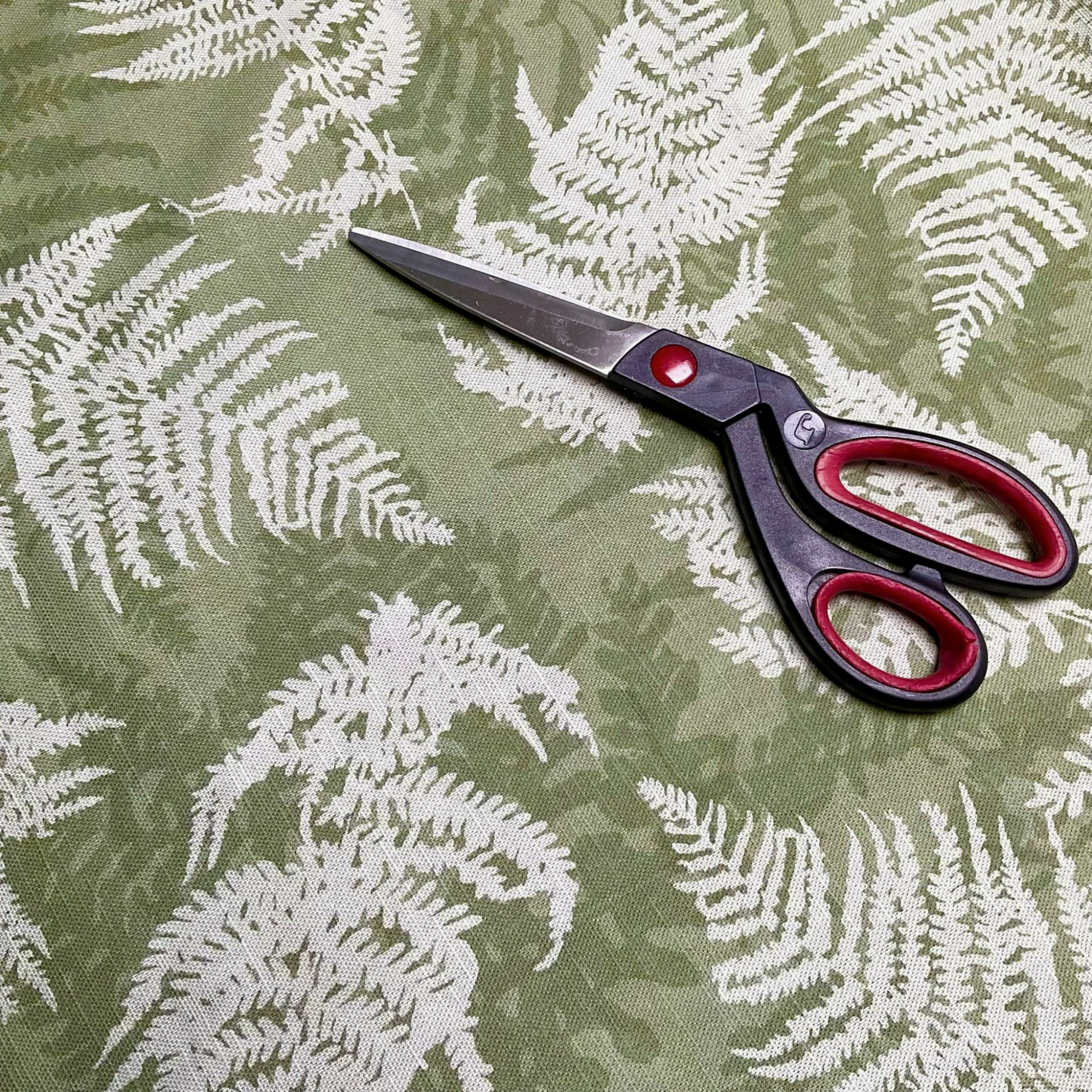 Green fabric with a fern print on and a pair of scissors is laid on the fabric