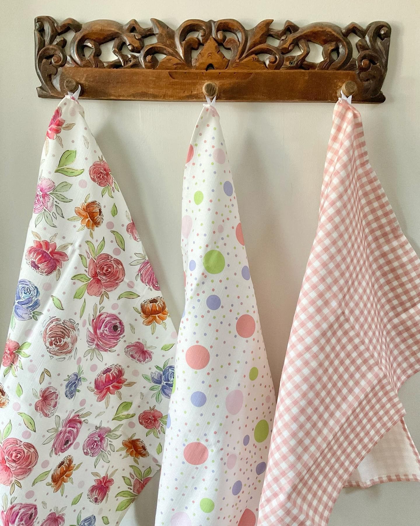 3 tea towels hanging on a rail. One has flowers on, one is polka dot and one is gingham