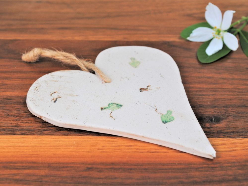Handmade ceramic hanging heart from white clay with green leave prints.