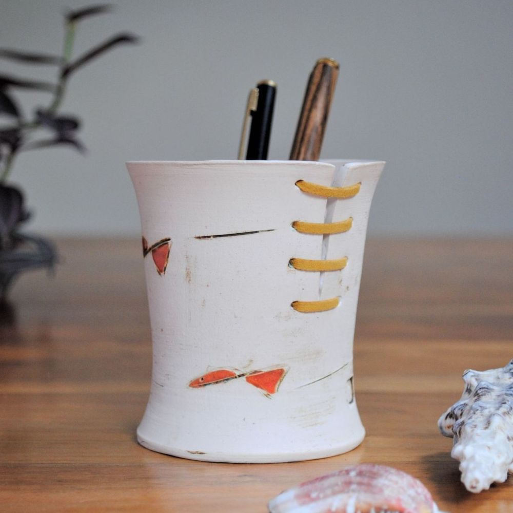 Handmade ceramic pencil holder from white clay decorated with orange fish. 