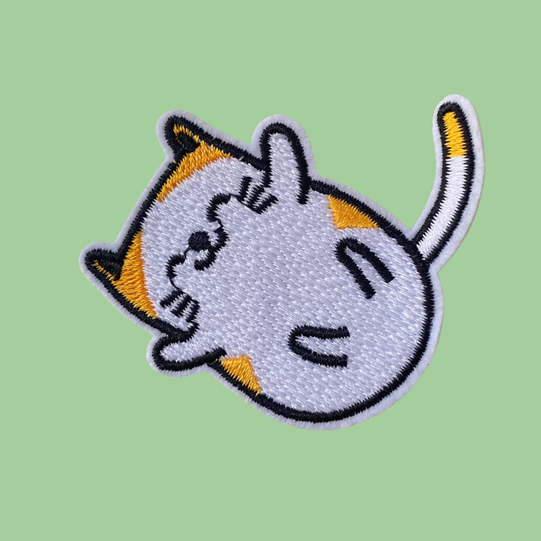 An Iron on patch of a happy cat rolling on a green background