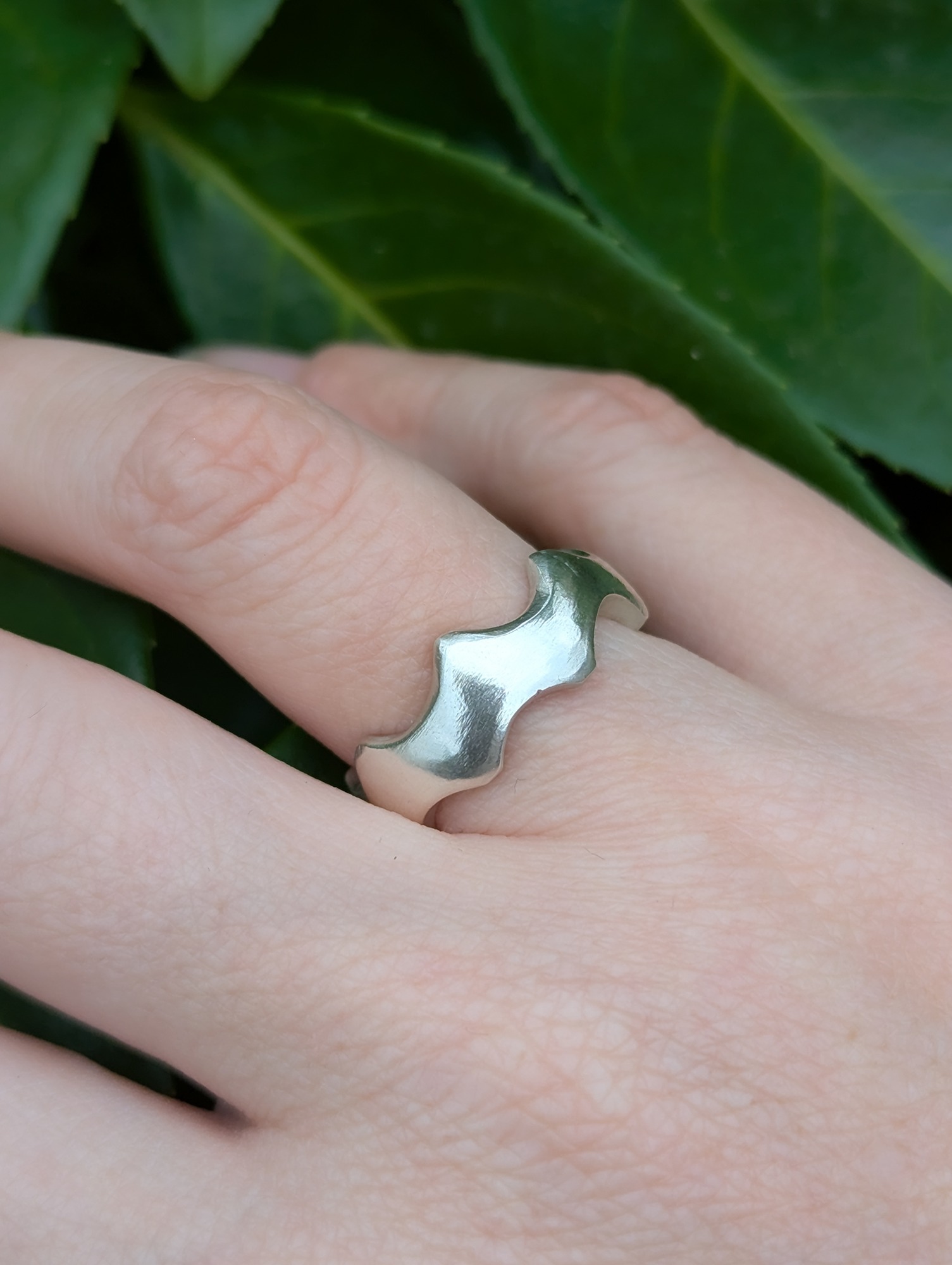 a close up of an abstract sterling silver crown ring being worn against a leafy back drop