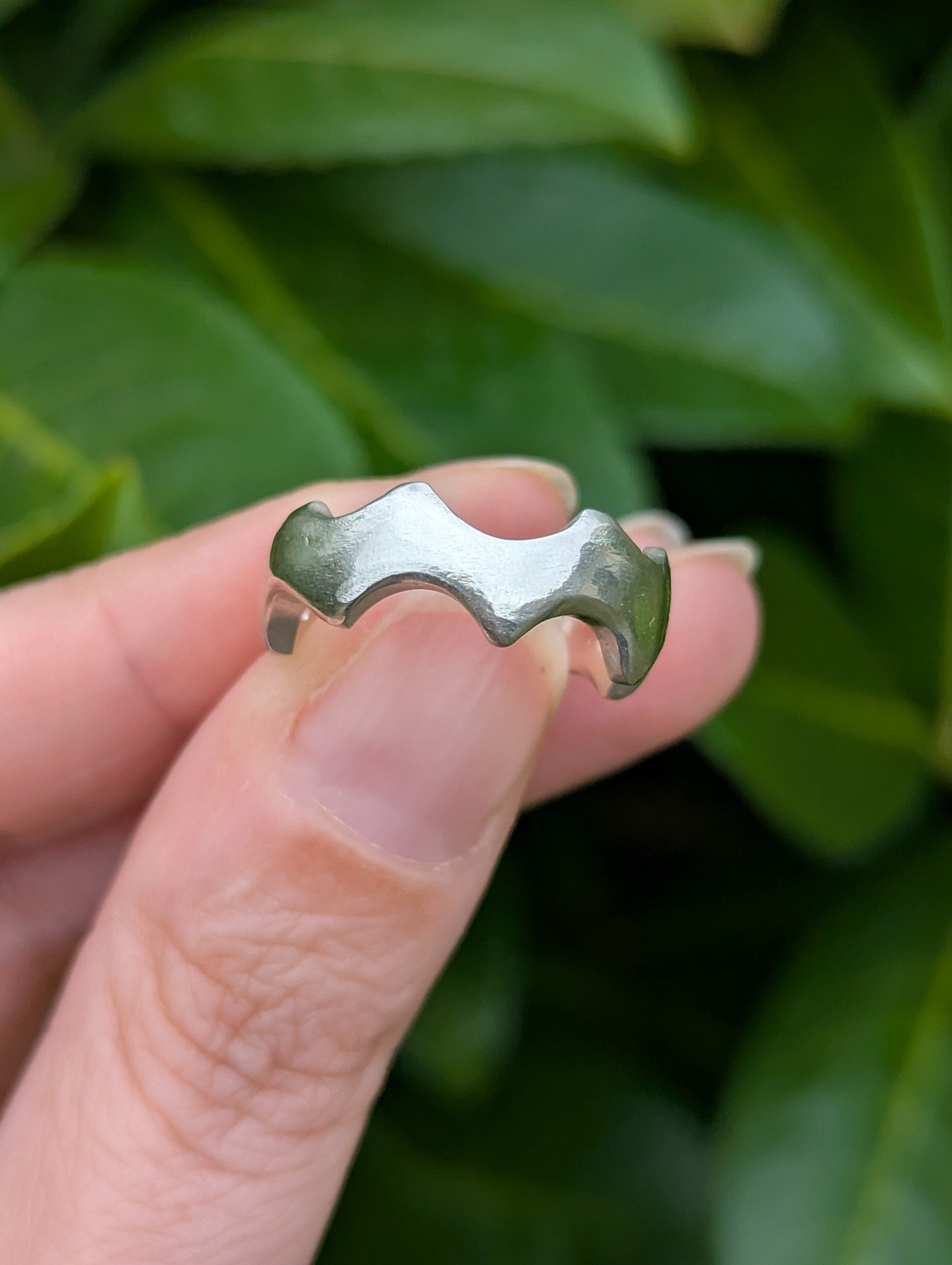 abstract sterling silver crown ring being held against a leafy back drop