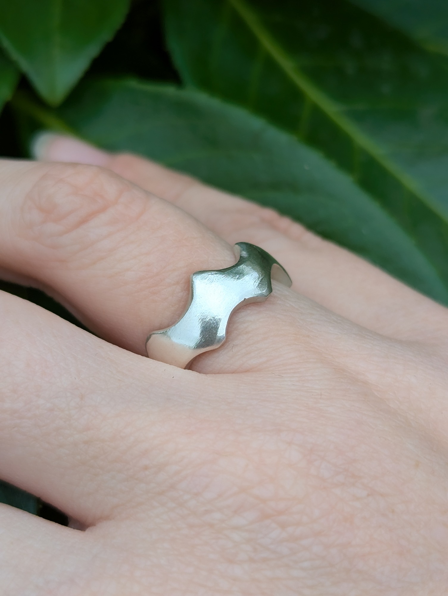 abstract sterling silver crown ring being worn against a leafy back drop