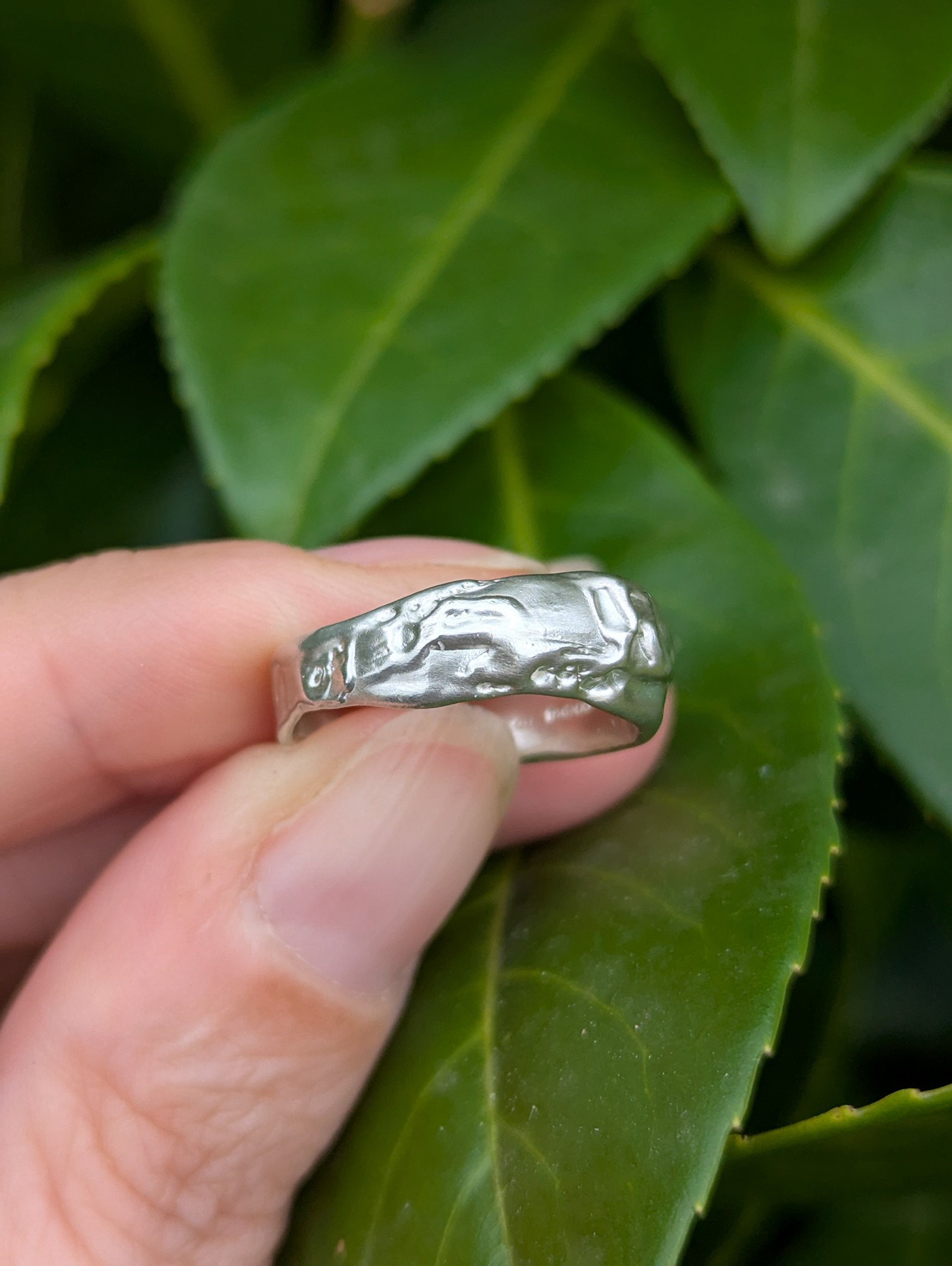 A sterling silver molten design ring being held against a green leafy backdrop