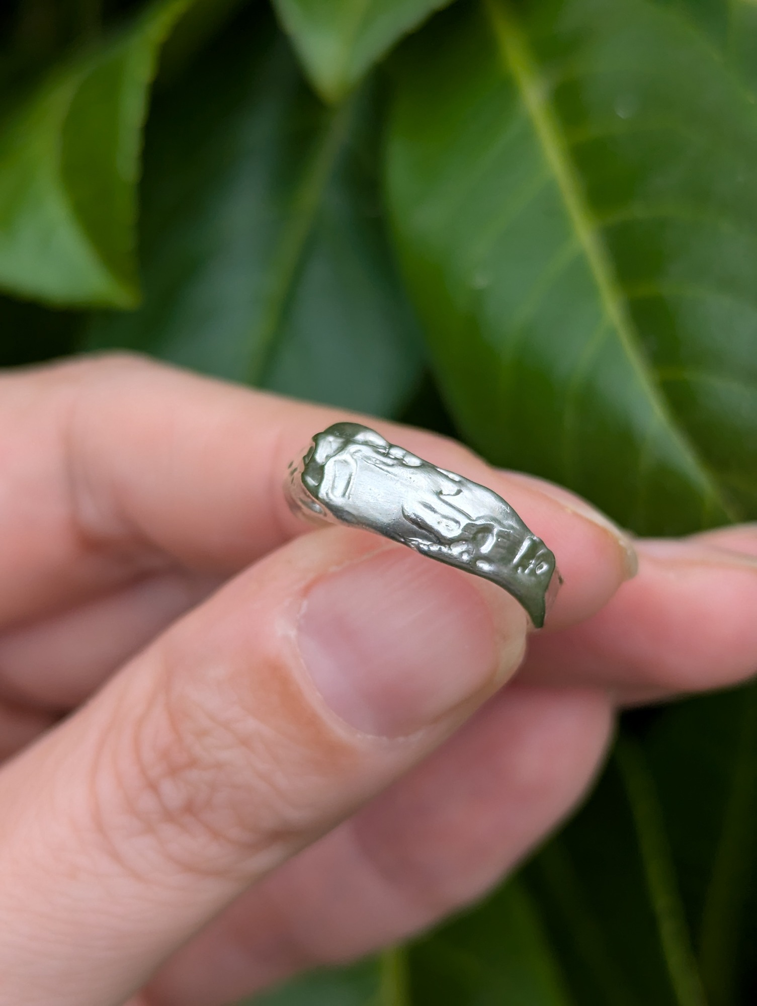 A sterling silver molten design ring being held against a green leafy backdrop