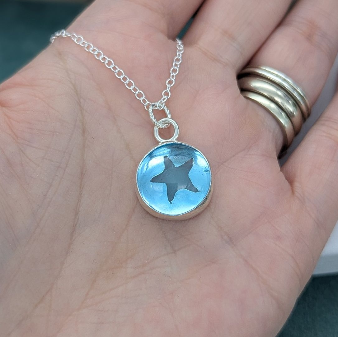 Aqua blue glass starfish necklace held on a hand