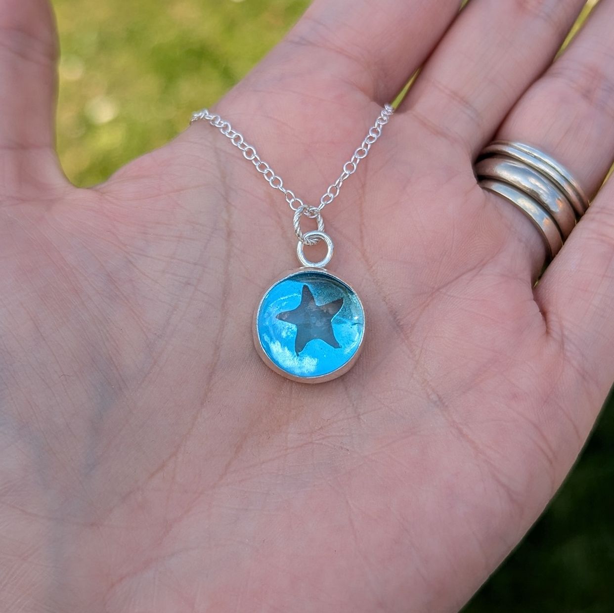 An aqua coloured glass pebble silver necklace with starfish cut out detail resting on a hand