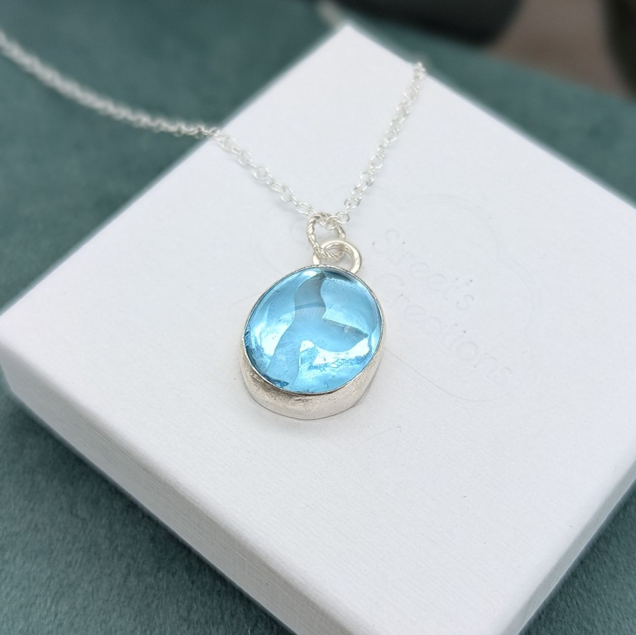Aqua blue glass whale tail cut out silver necklace on a white jewellery box