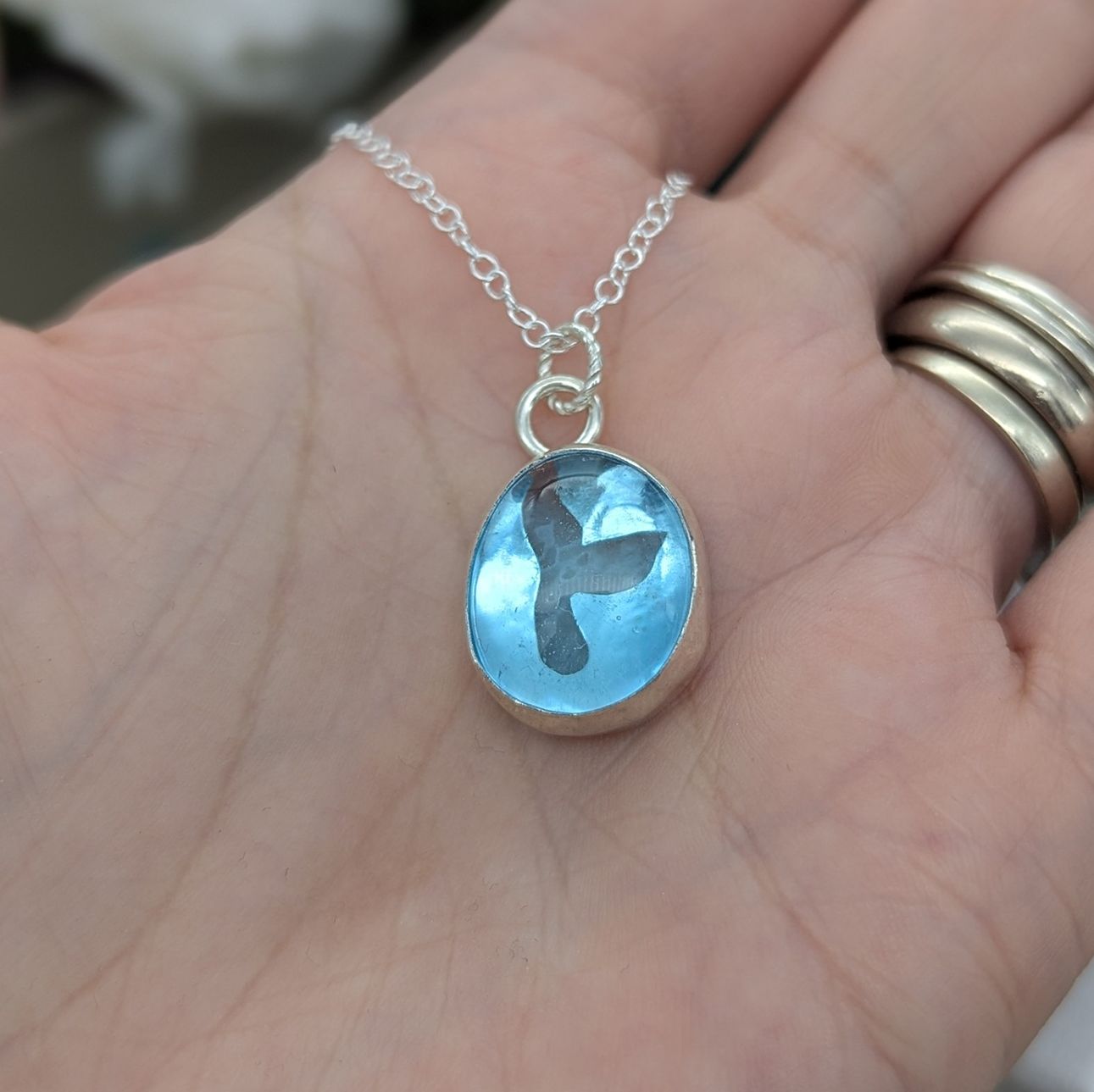 A blue aqua glass pebble silver necklace with a whale tail cut out detailing 