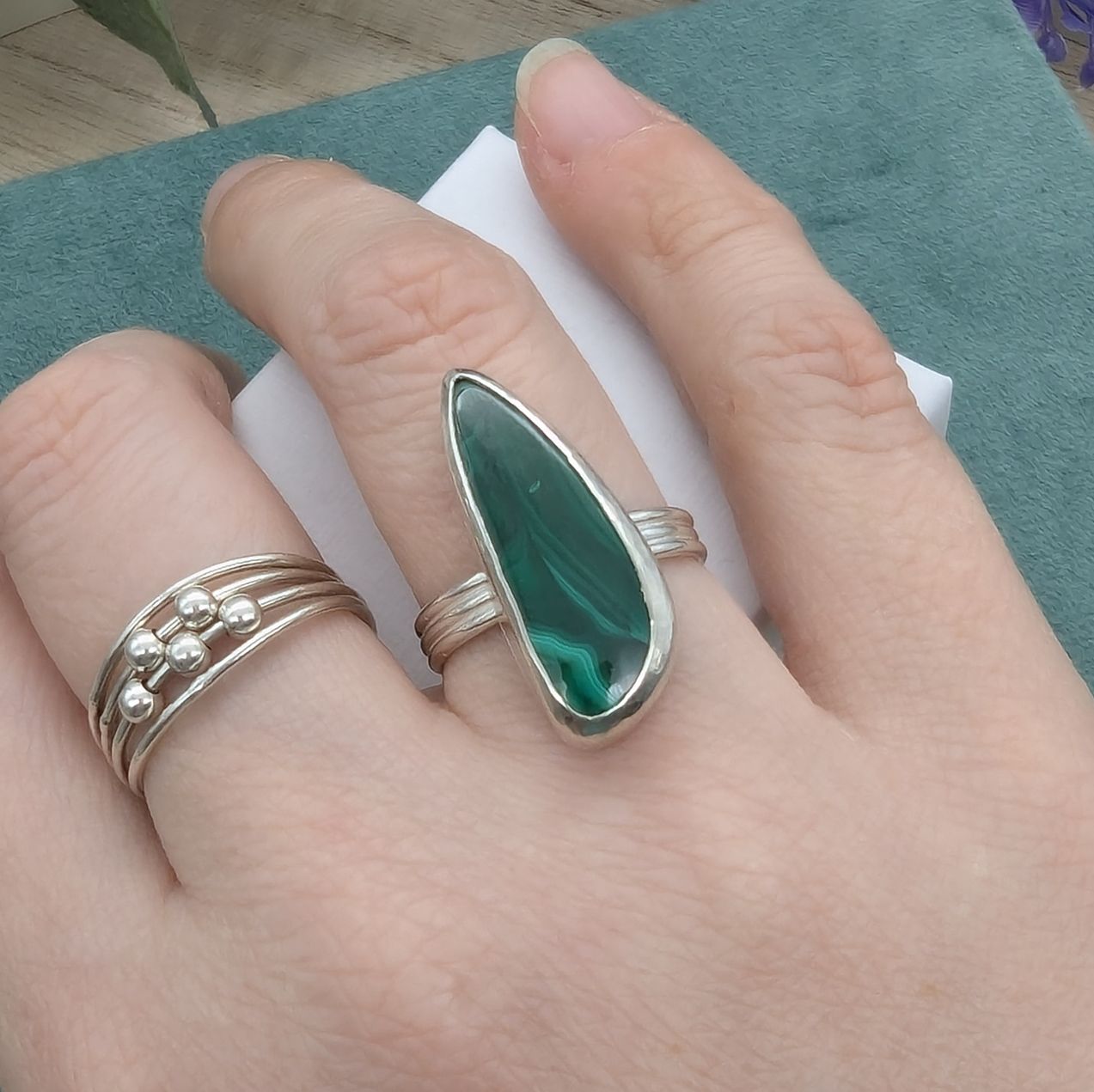 A freeform malachite gemstone and silver ring being modelled on a hand next to a silver fidget ring