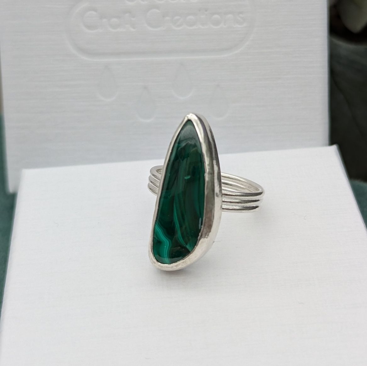 A freeform Malachite gemstone ring resting on a white jewellery box 