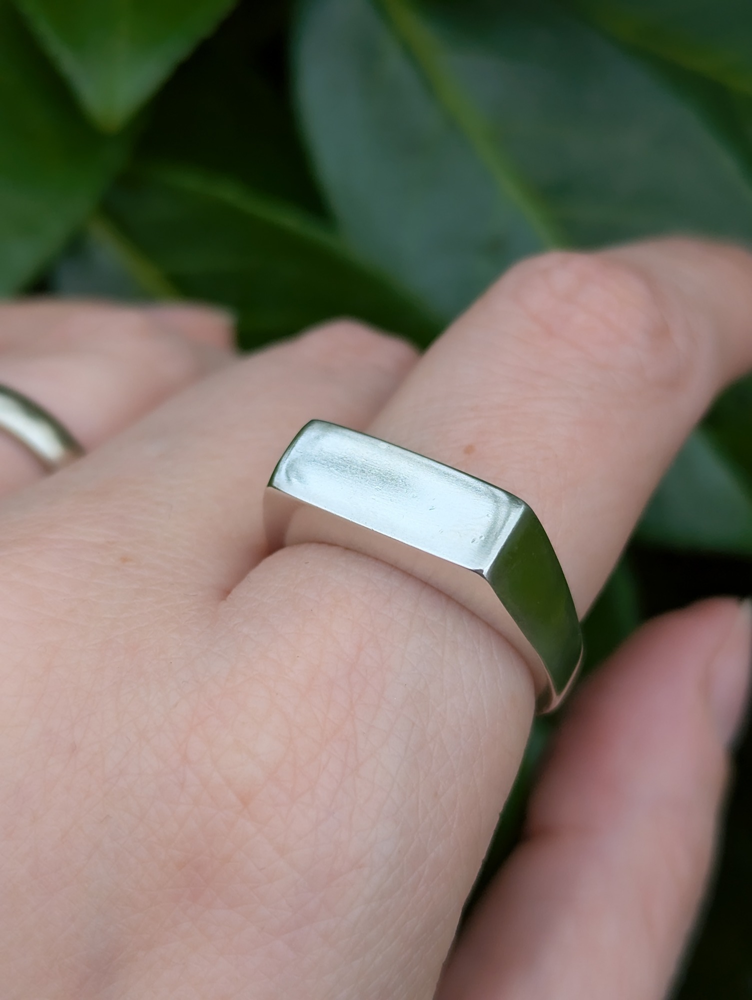 Sterling silver rectangle signet ring being worn against a leafy backdrop