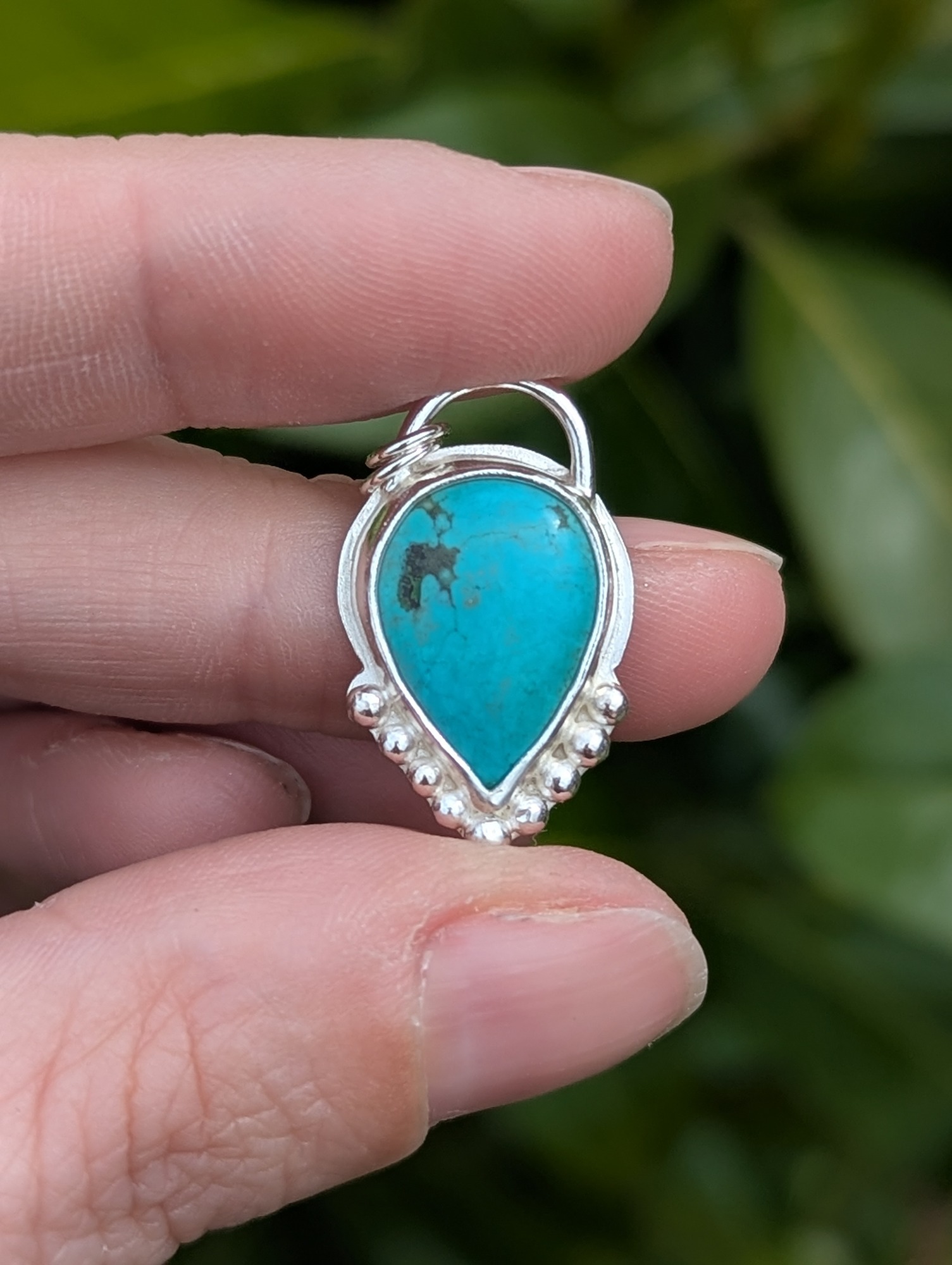 Turquoise and silver necklace with granulation detail being held between two fingers