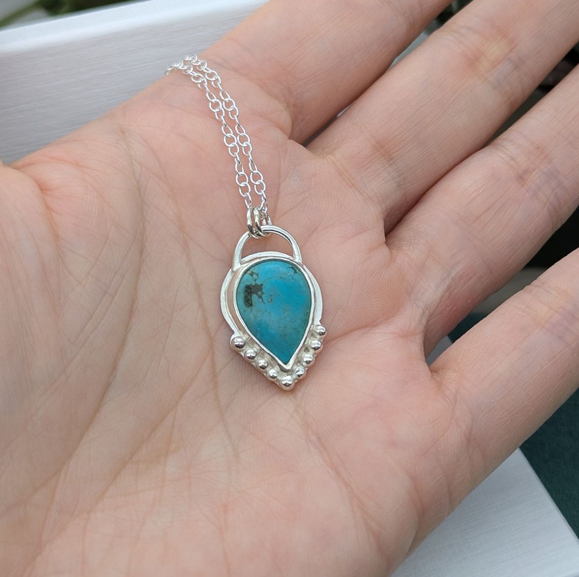A sterling silver & Turquoise necklace being held in the palm of a hand 