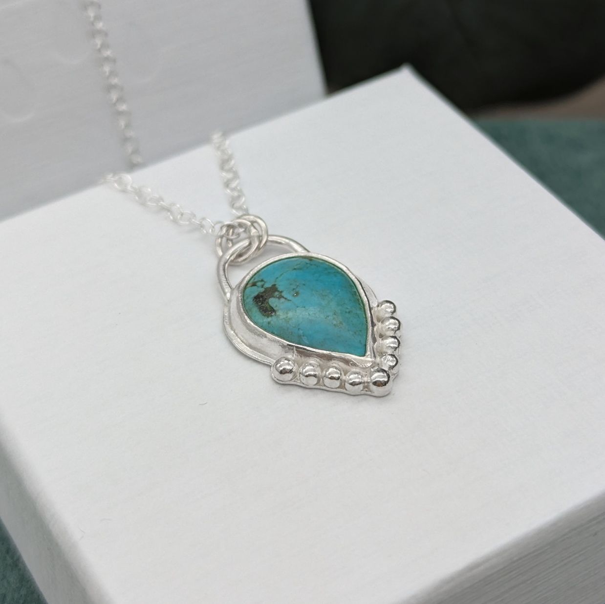 Side view of a silver & turquoise necklace resting on white jewellery box