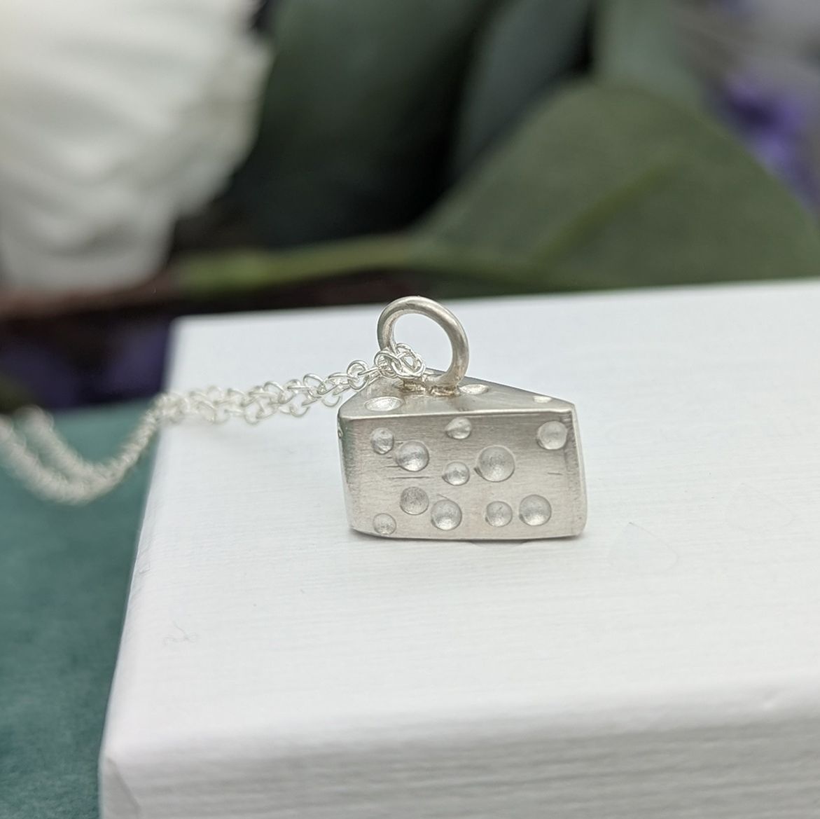 Sterling silver cheese wedge shaped necklace resting on a white jewellery box