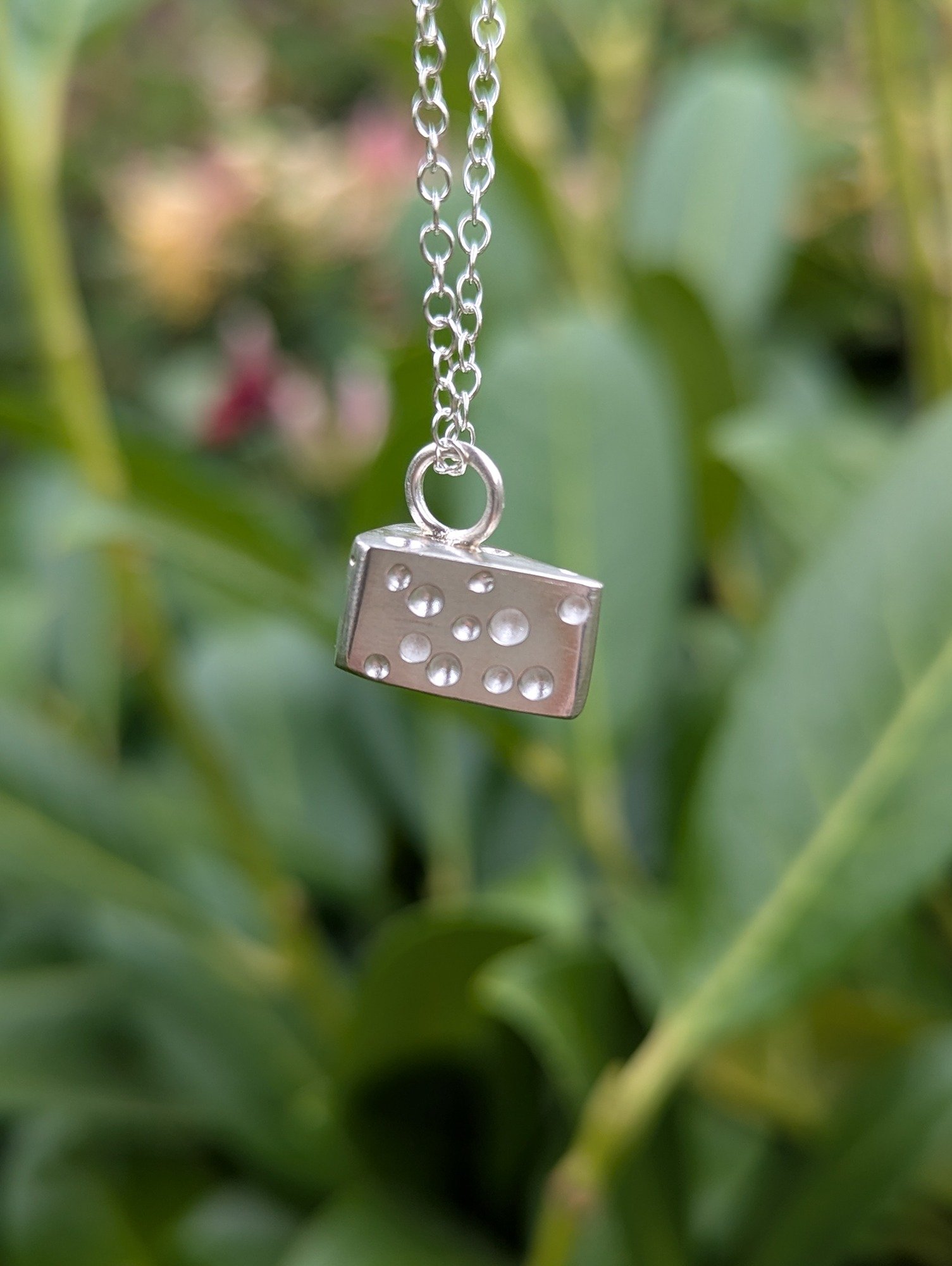 a sterling silver cheese wedge necklace hanging in front of leafy backdrop