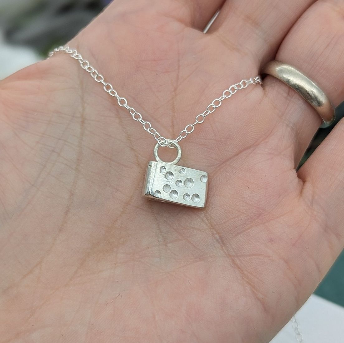 Side view of the silver cheese necklace resting in an open palm of a hand