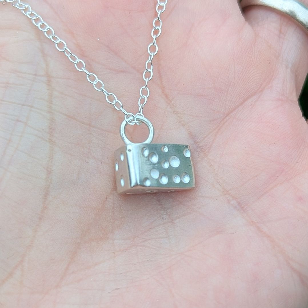 Side view of the silver cheese wedge necklace resting on the palm of a hand