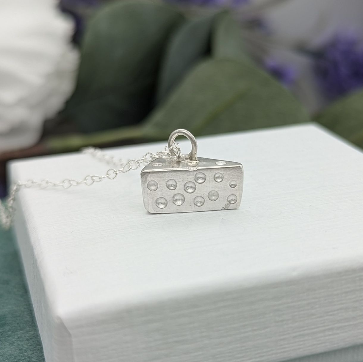 a sterling silver cheese shaped necklace resting on a white jewellery box